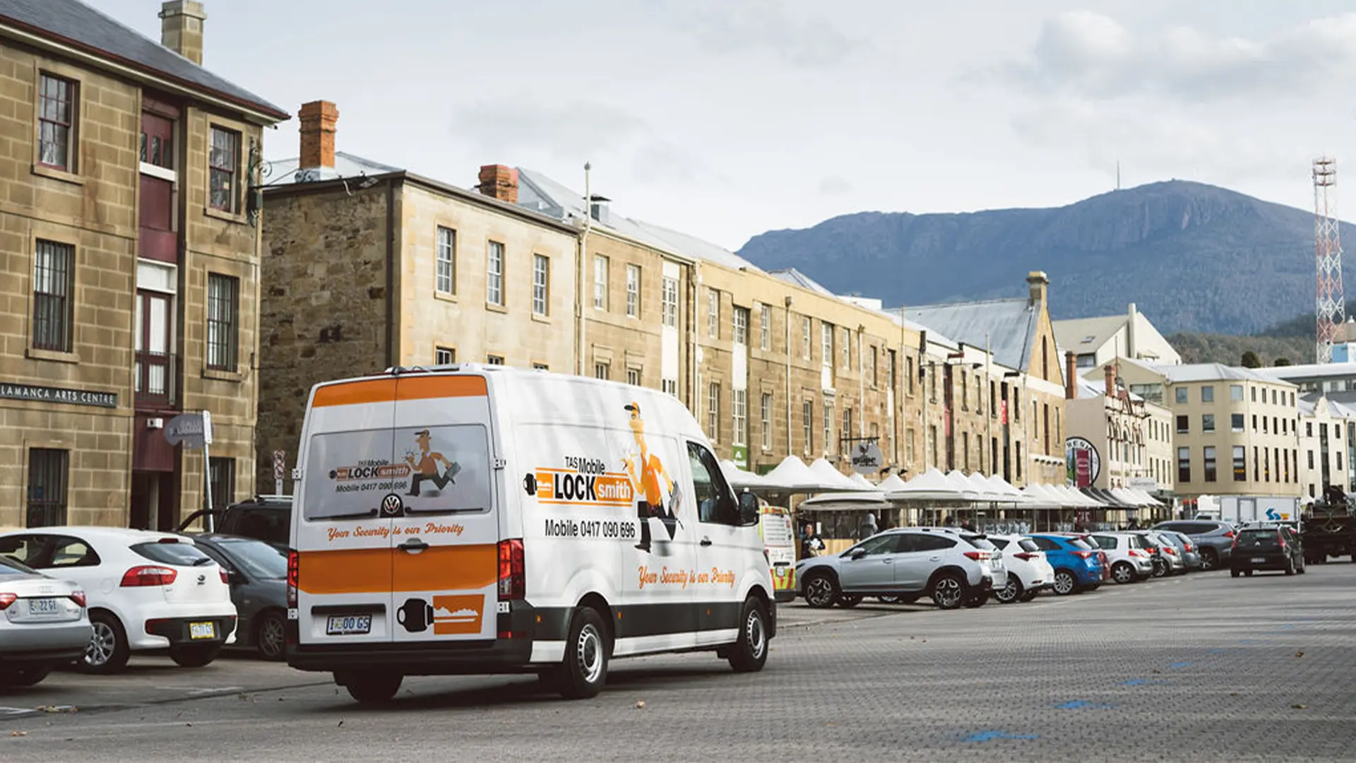 White and orange locksmith van parked on street with historic buildings and mountain