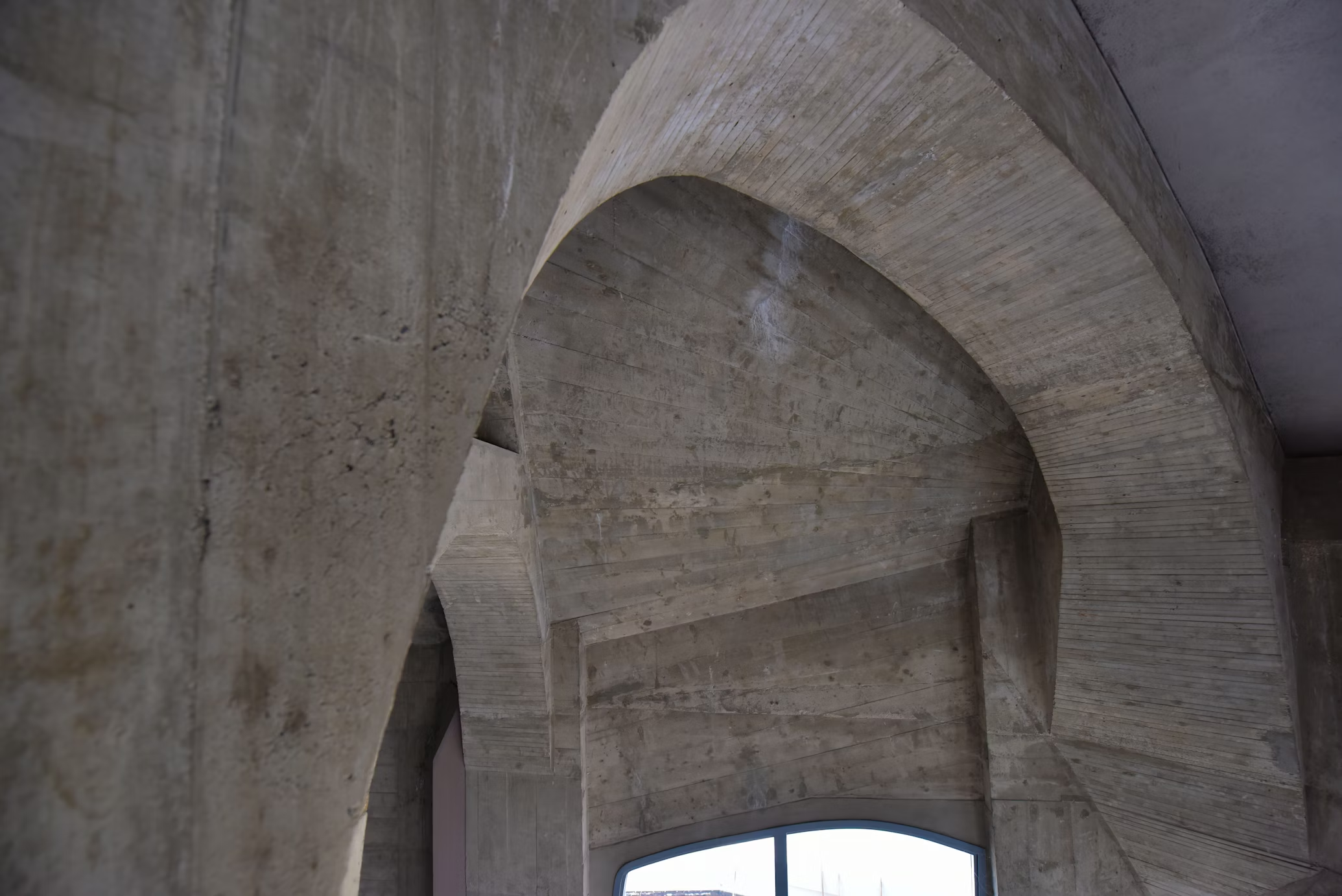 Interior view of a building showing large, curved concrete architectural elements near a window.