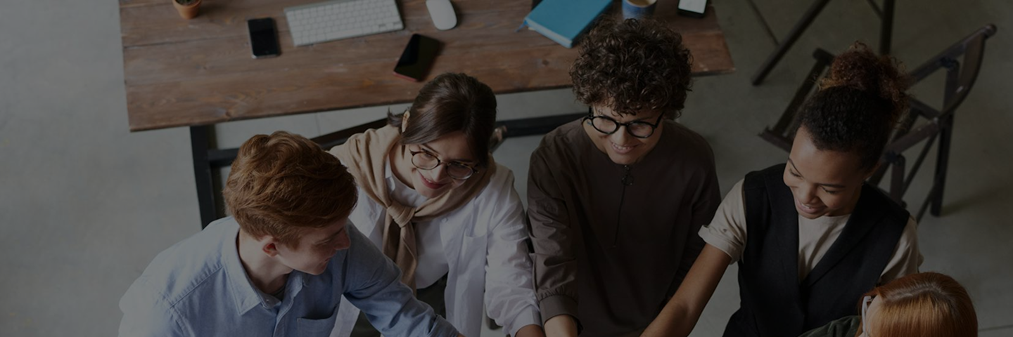 Five diverse young adults sitting at a table, smiling and collaborating together on a project.