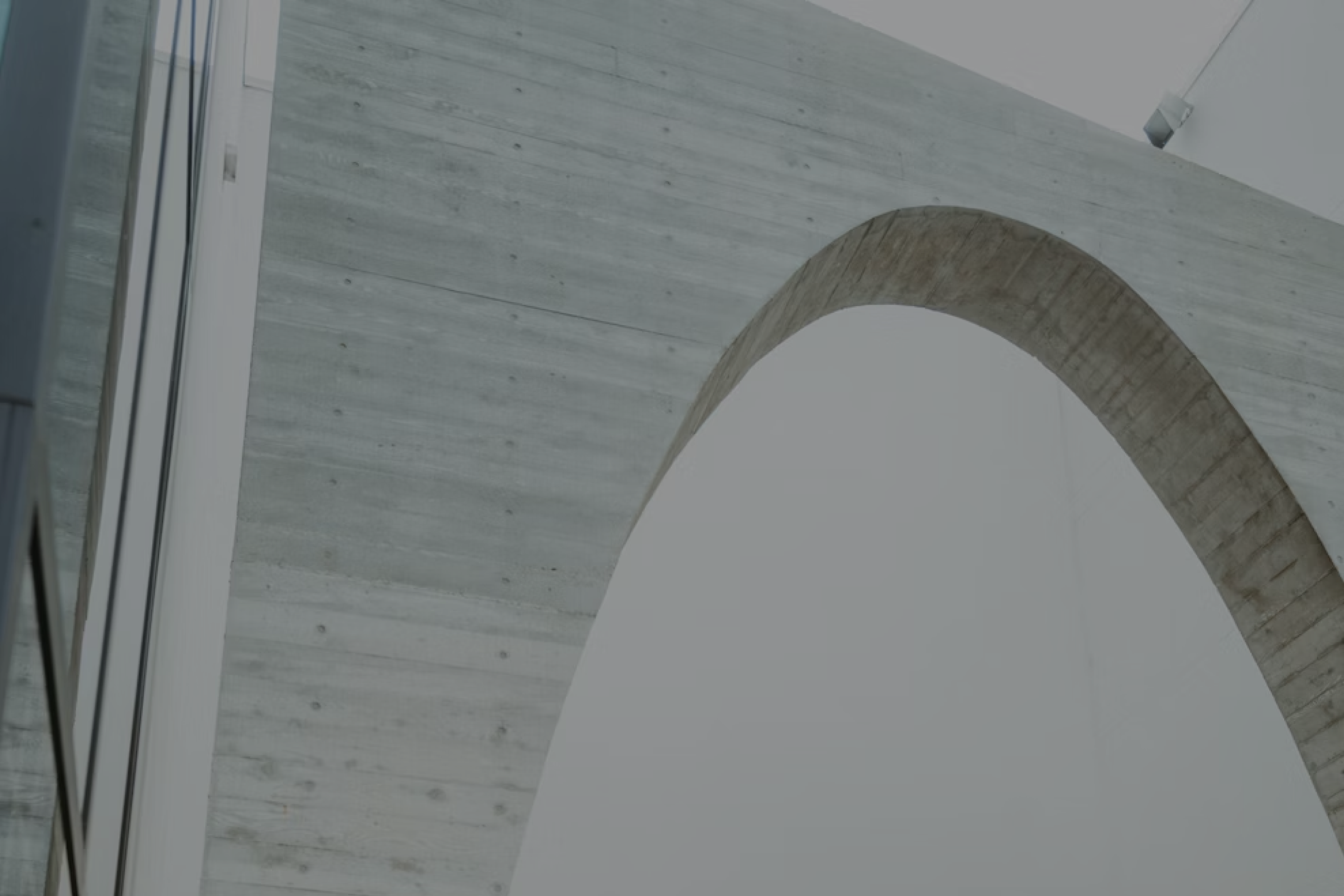 Curved concrete arch inside a modern building featuring smooth grey surfaces and glass windows.