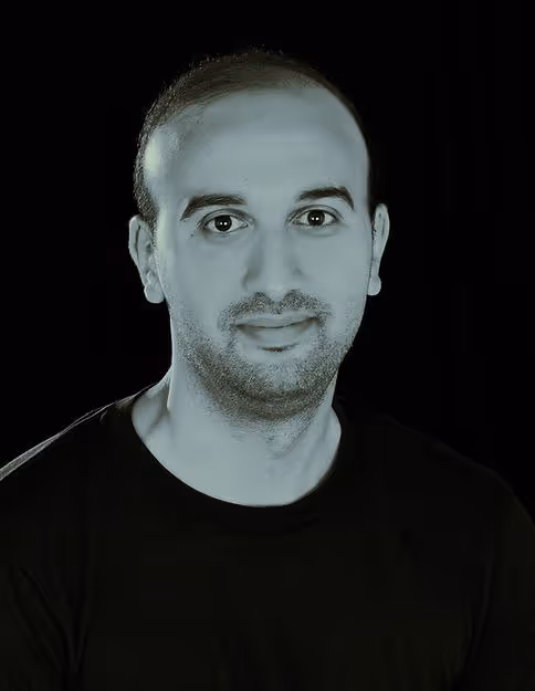Portrait of a man with short hair and beard wearing a black shirt against a black background.