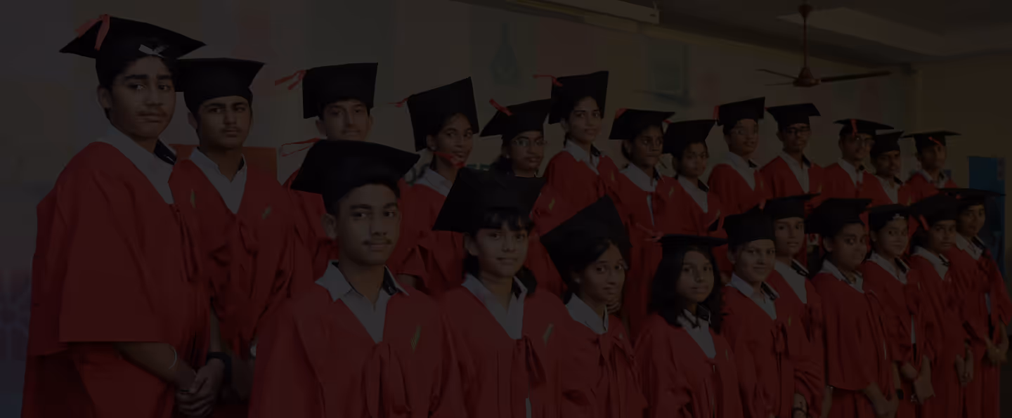 Group of students in red graduation gowns and black caps standing indoors in a classroom.