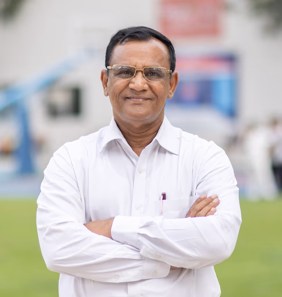 Middle-aged man wearing glasses and a white shirt stands outdoors with arms crossed, smiling.