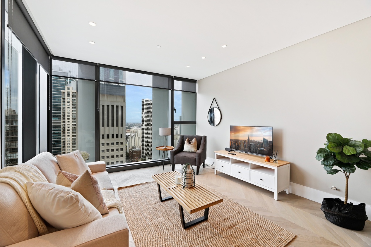 Modern open-plan kitchen and living area with wooden cabinets, glass doors, dining table, and indoor plants.