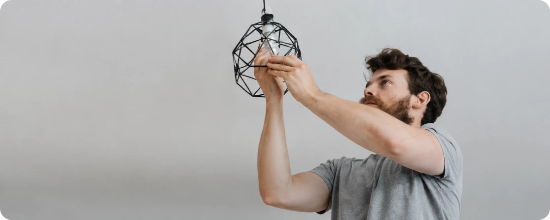Man in grey t-shirt adjusting or installing a modern geometric black pendant light fixture.
