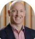 Smiling bald man wearing a dark blazer over a pink shirt.