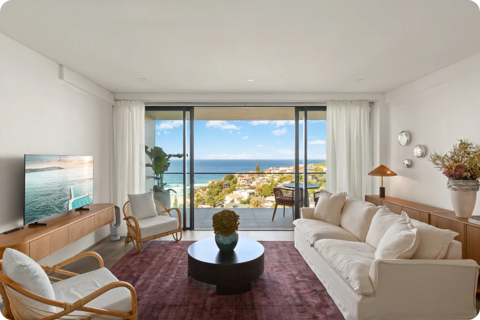 Outdoor balcony lounge with cushioned wooden sofas, potted plants, hanging lantern, and city view.