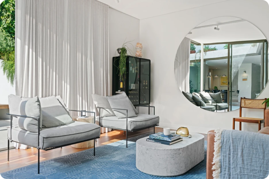 Modern bedroom with king bed, blue bench, armchair, balcony, and ocean view through floor-to-ceiling glass.