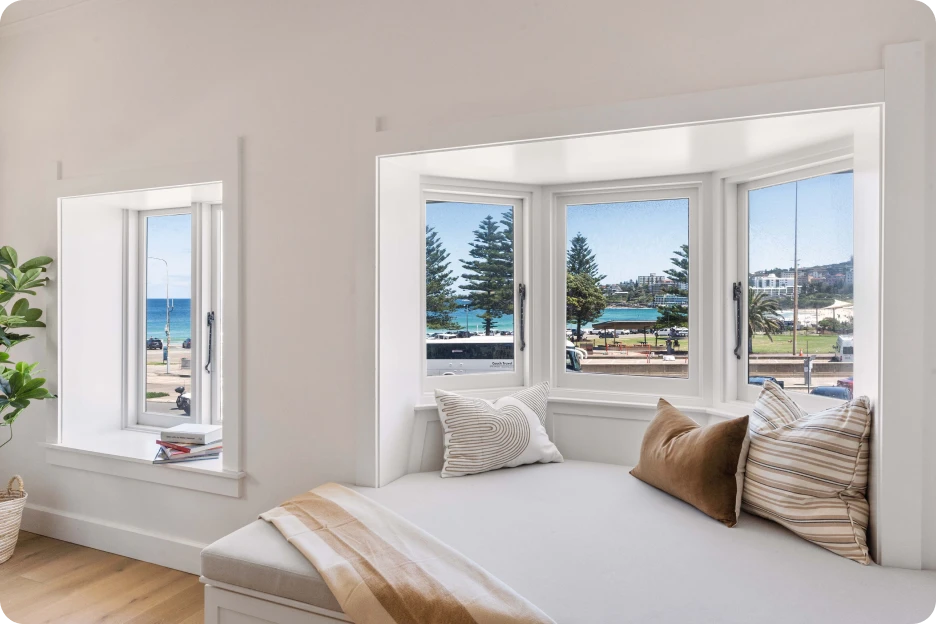 Modern bedroom with white bed, grey pillows, black nightstands, and glass partition wall.