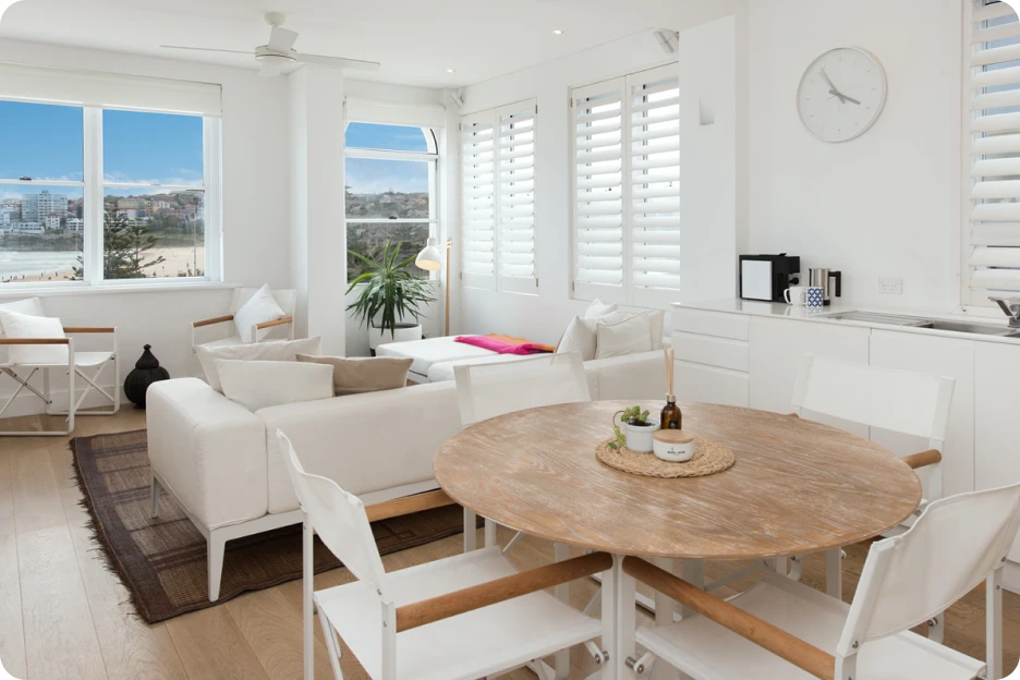 Modern living room with glass walls, a TV, two armchairs, sofa with cushions, and plants inside and outside.