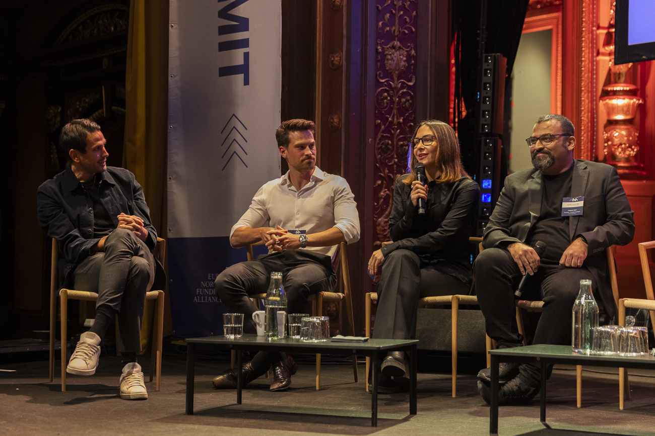 Four people seated on stage during a panel discussion, with one woman speaking into a microphone.