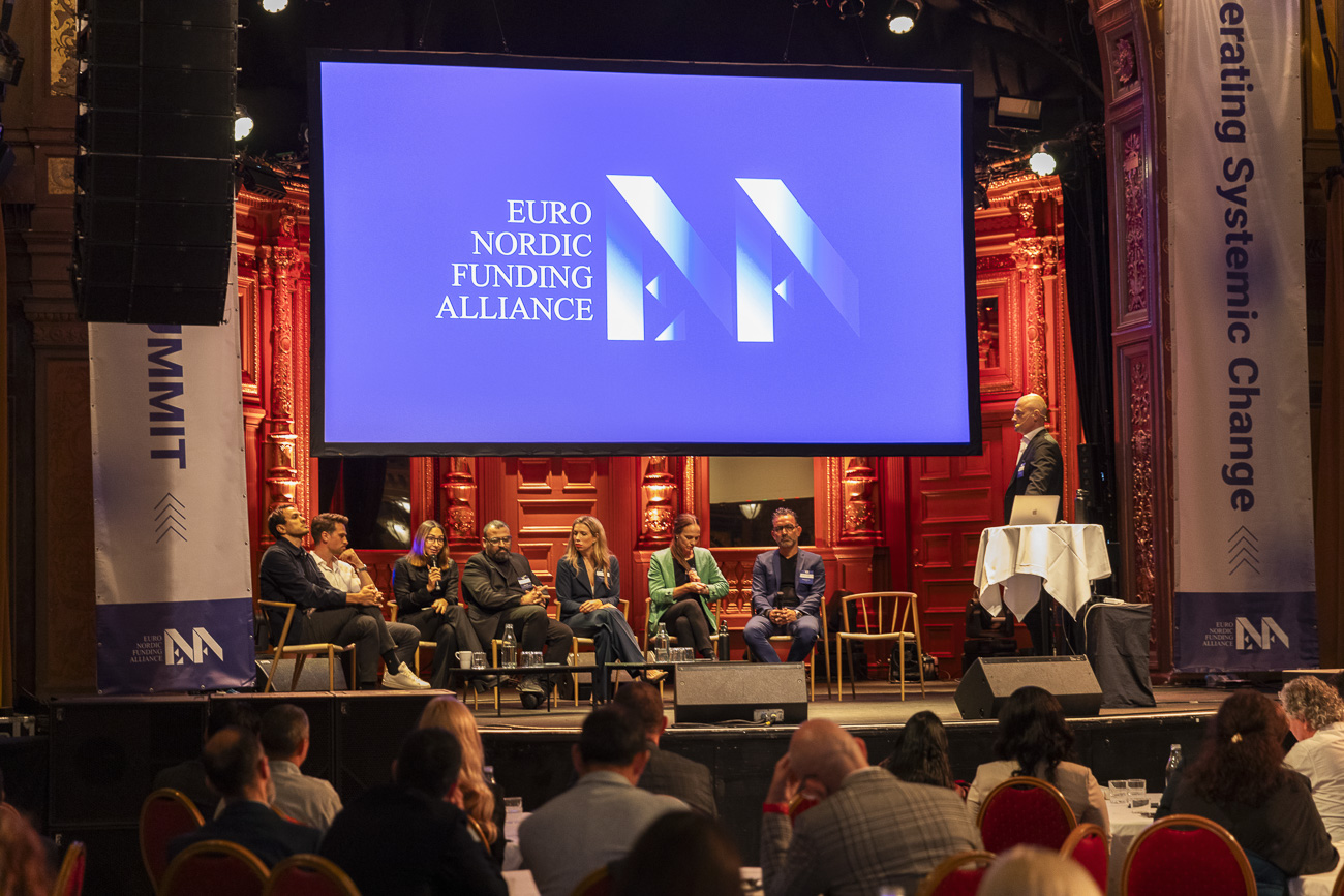 Panel of seven speakers seated on stage under a large screen displaying 'Euro Nordic Funding Alliance' logo, with an eighth person standing at a podium.
