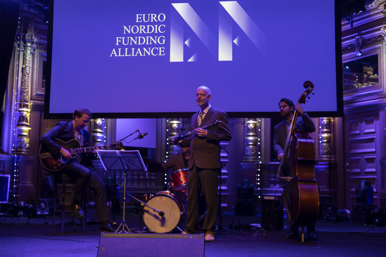 Jazz quartet performing on stage under a large screen displaying the Euro Nordic Funding Alliance logo in an ornate venue.