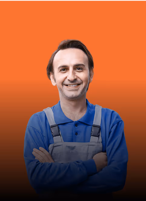 Lächelnder Mann in blauer Arbeitskleidung vor orangem Hintergrund, verschränkte Arme.