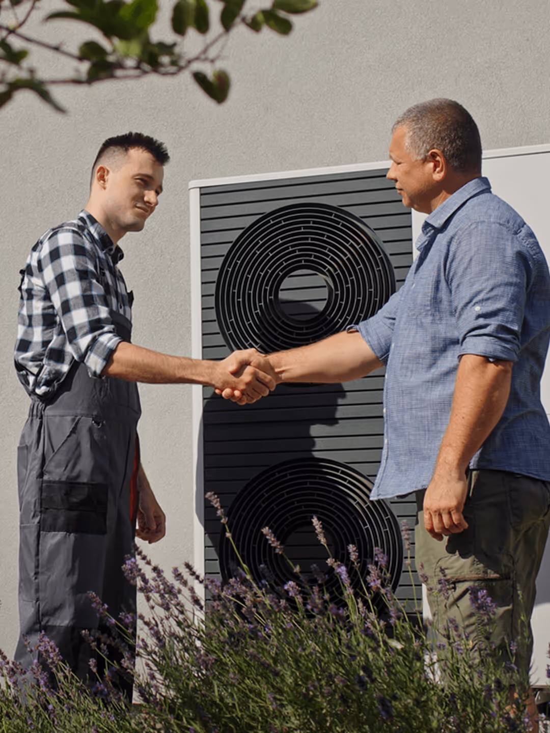 Zwei Männer schütteln sich die Hand vor einer Wärmepumpe im Freien, umgeben von Lavendel.