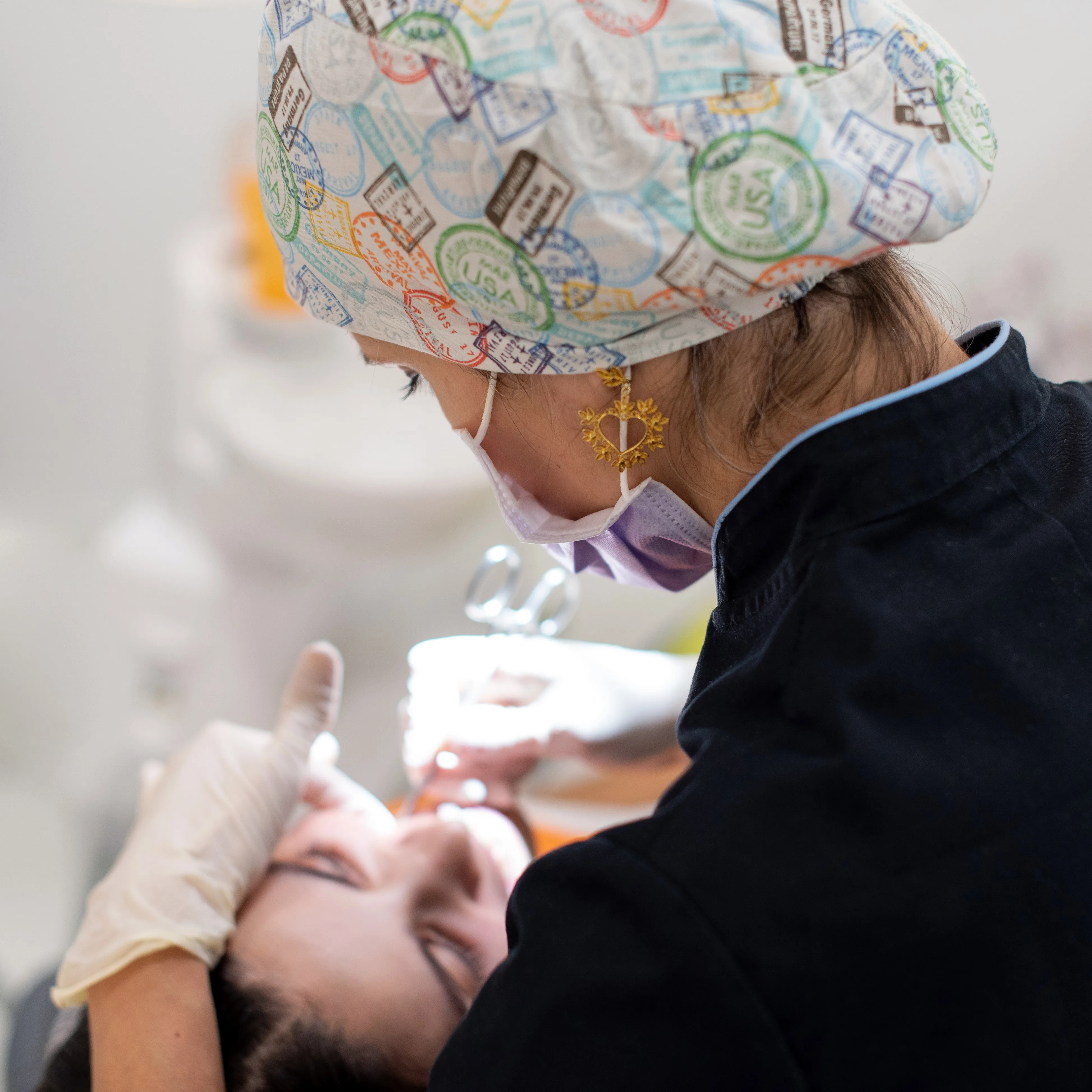 Dentista usando touca colorida e máscara realiza procedimento dental em paciente reclinado.