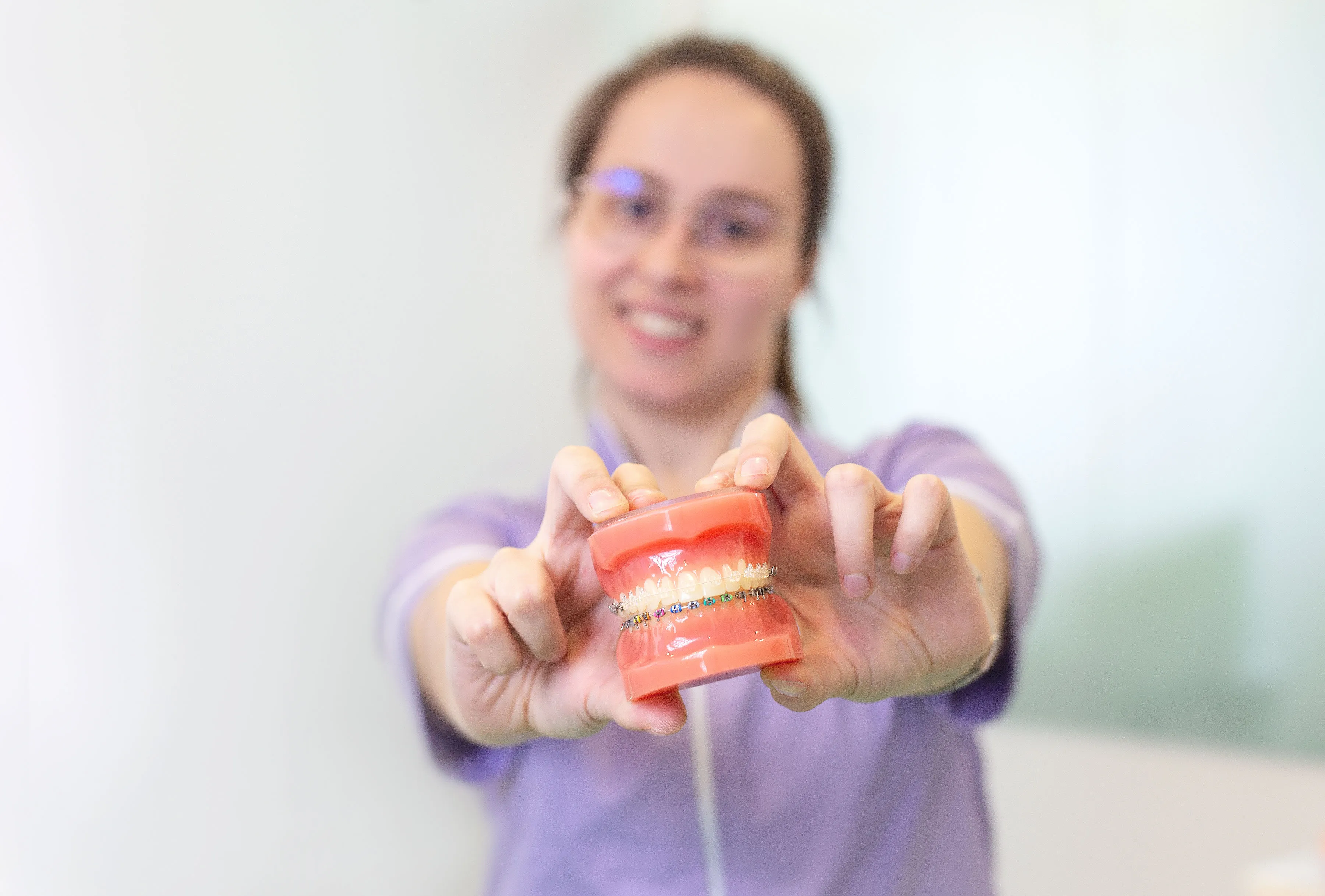 Médica dentista sorridente enquanto segura um modelo de dentes com aparelho ortodôntico colorido.