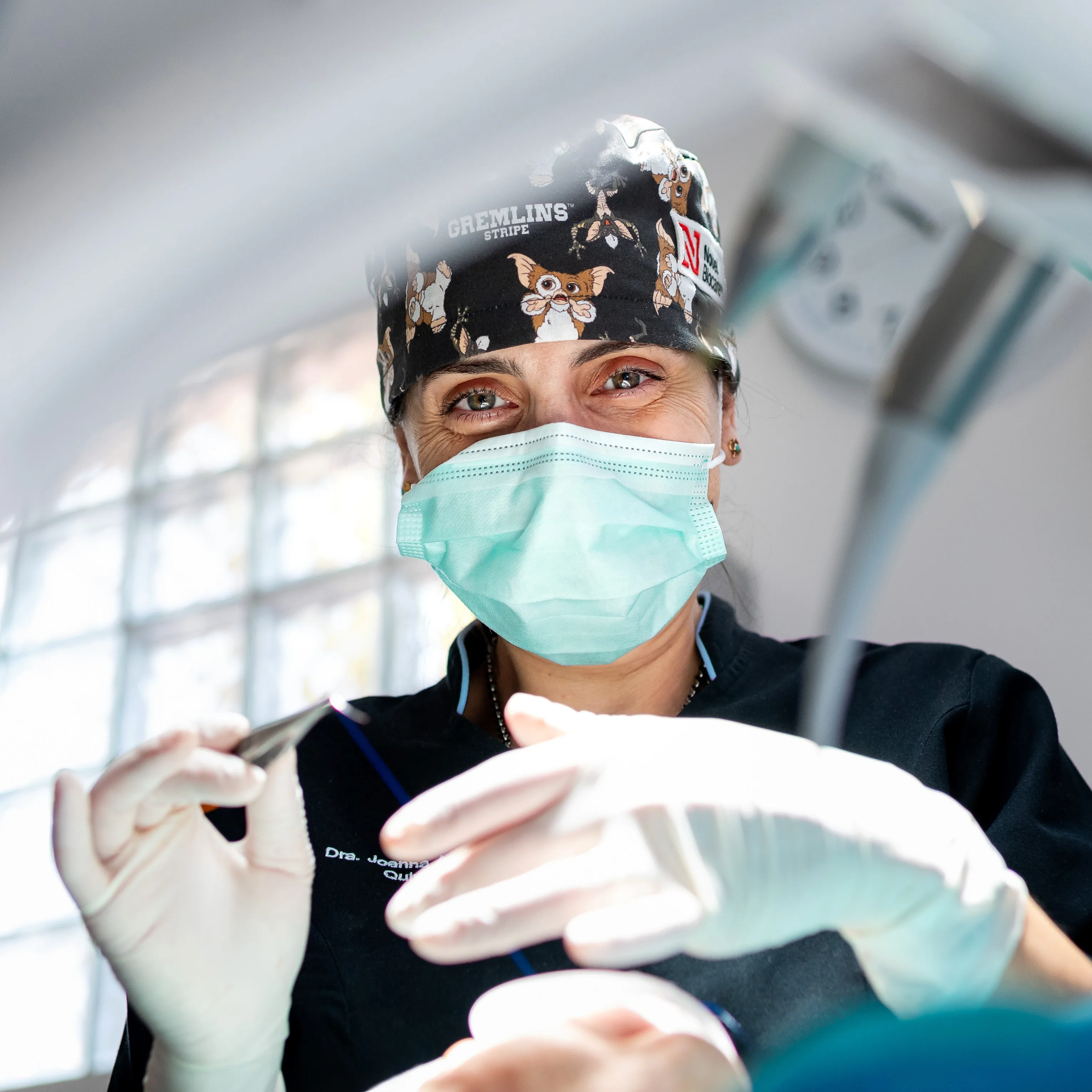 Dentista de máscara cirúrgica e touca sorrindo enquanto segura instrumentos durante o procedimento.