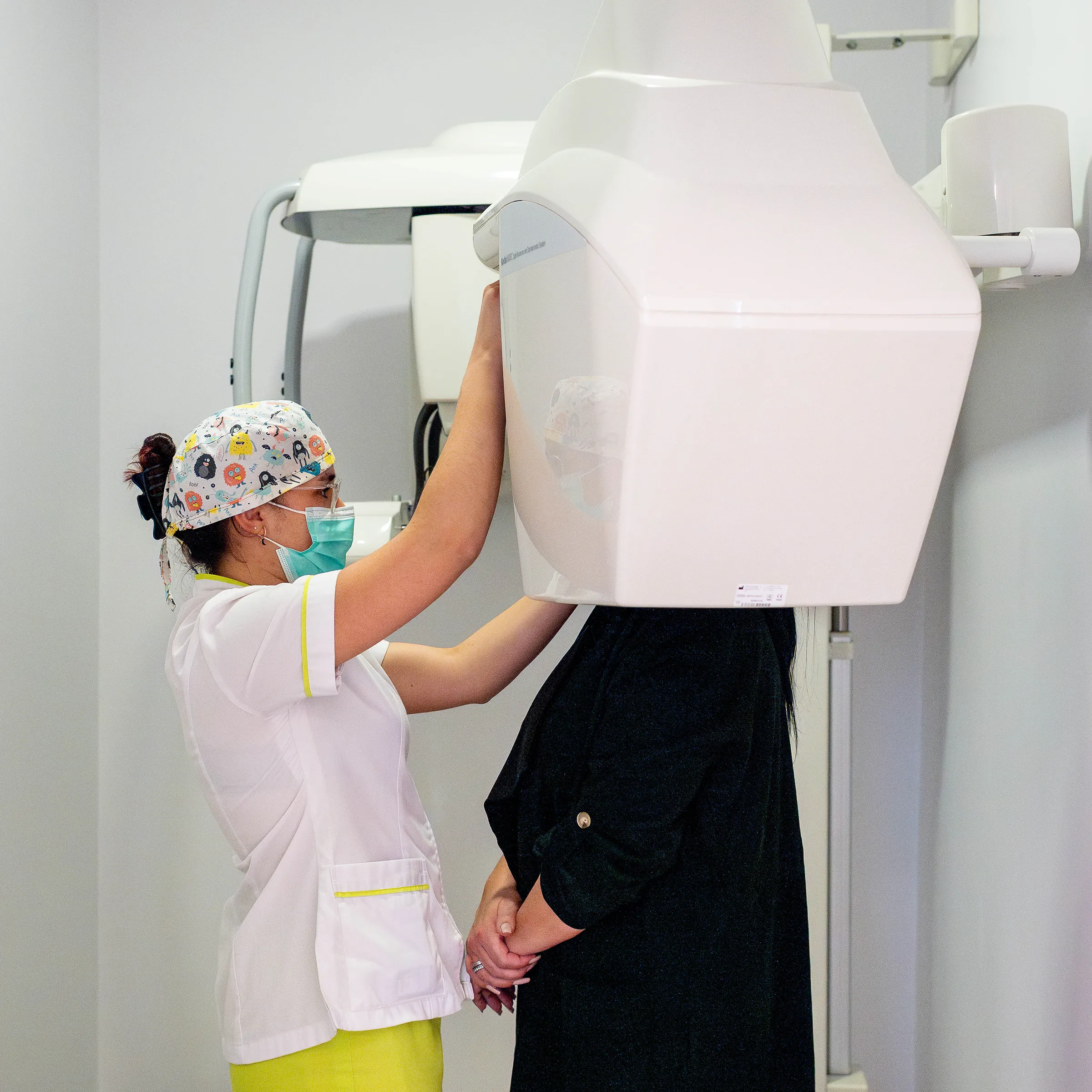 Técnica de saúde com máscara ajusta a máquina de raio-x para paciente em posição.