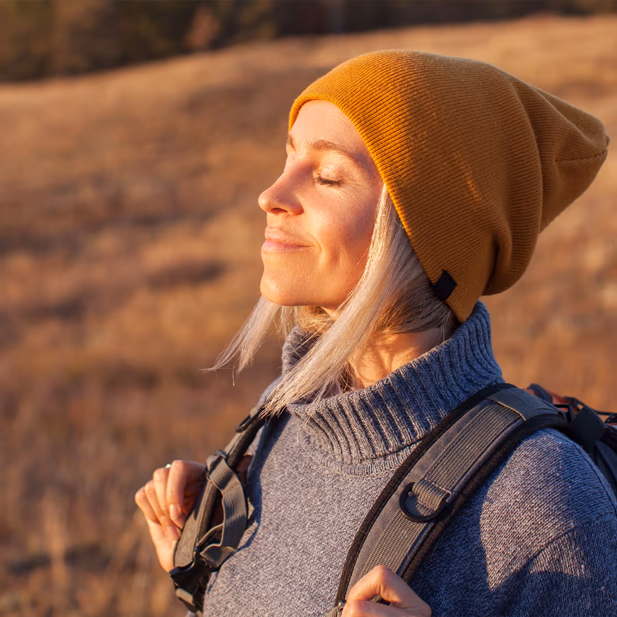 Serene middle aged woman enjoying sun on her face whilst hiking