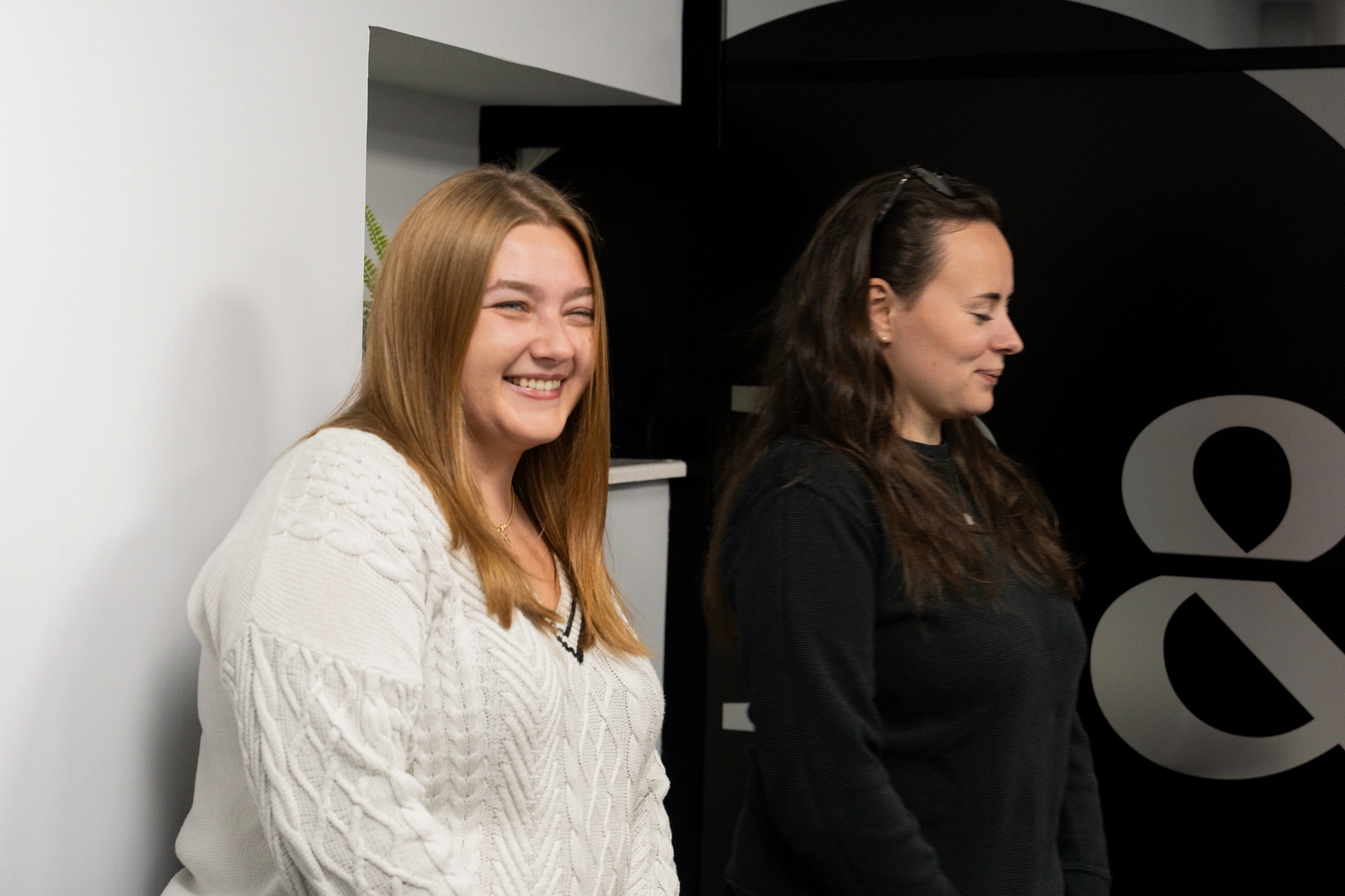 Agne and Jess talking with colleagues and exchanging smiles and laughter, part of the day to day life at Black and White Bridging.