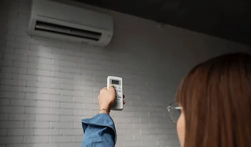 Person adjusting air conditioning remote control near wall-mounted unit