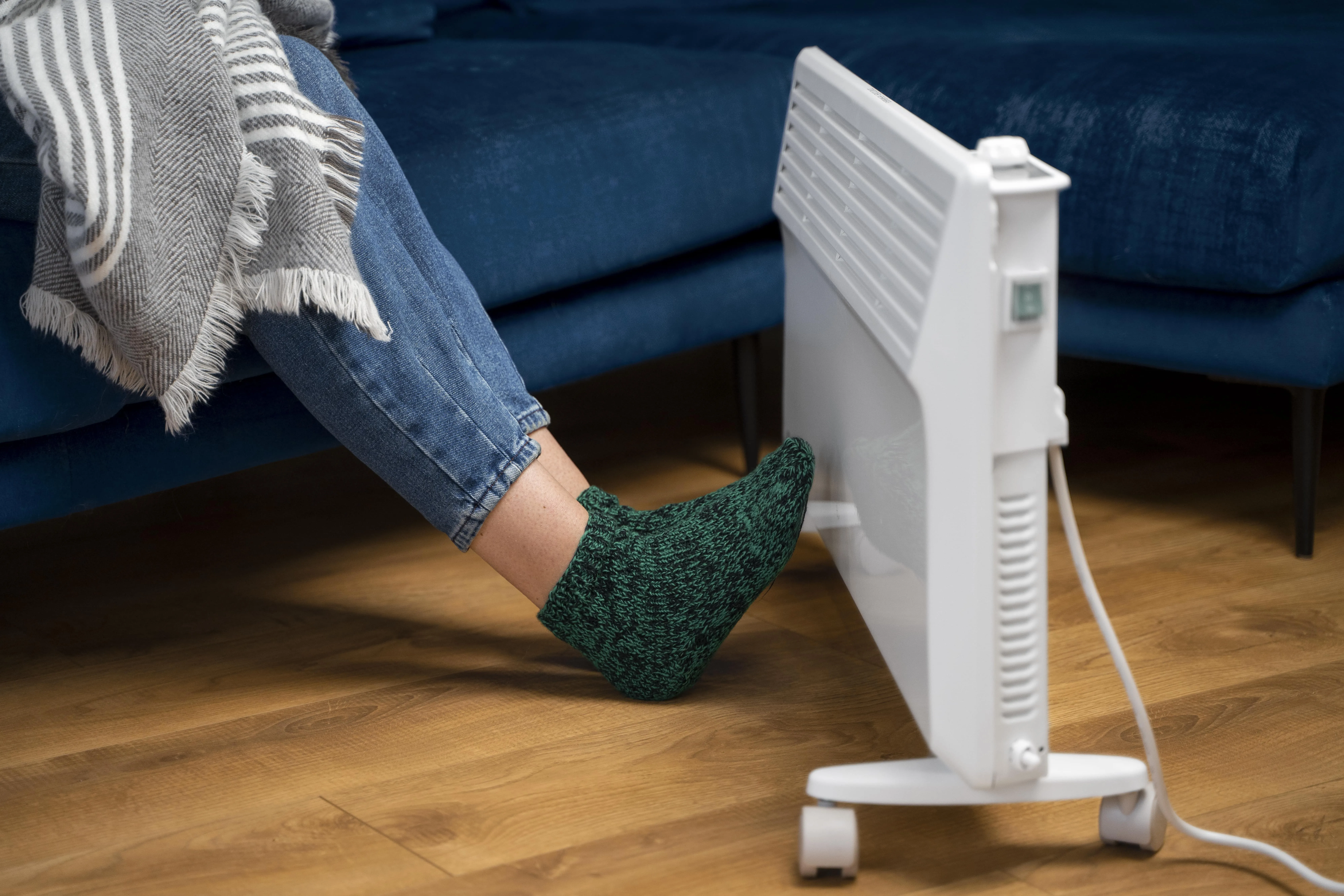 Person in jeans and green sock warming foot near electric heater