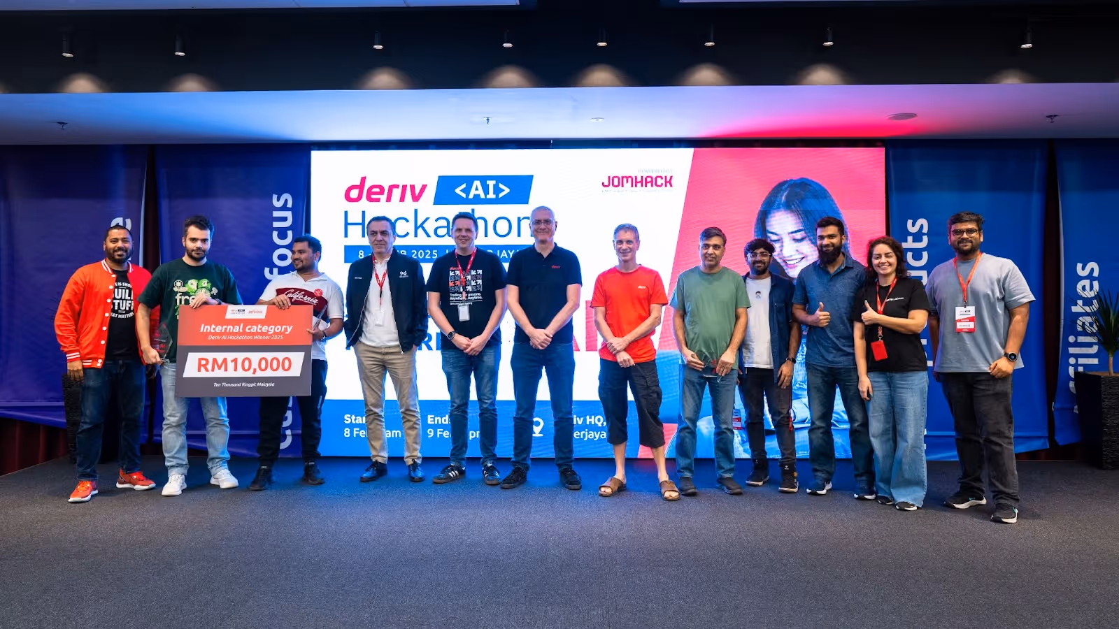 Internal innovation winners from the second AI Hackathon at Deriv standing on stage, holding a prize cheque, celebrating their achievement.