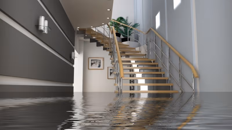 Überfluteter moderner Innenraum mit einer Holztreppe und reflektierendem Wasser auf dem Boden.