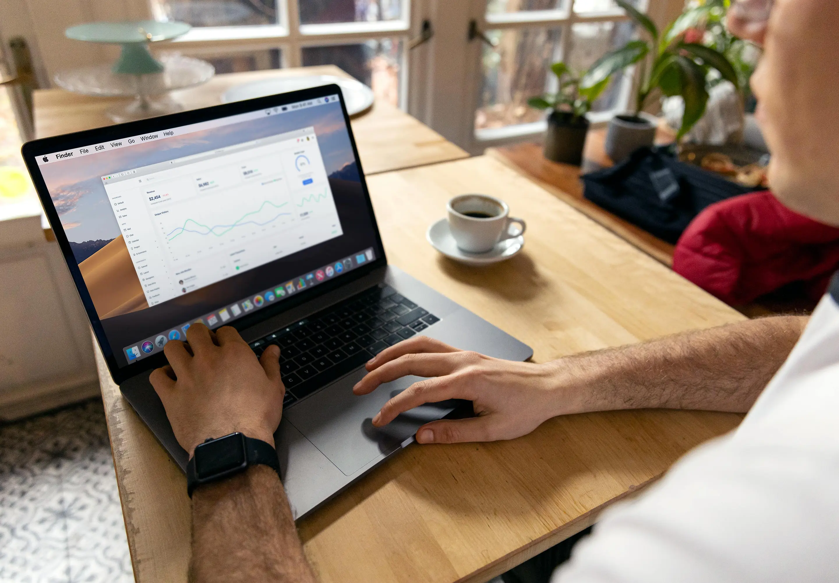 Person using a laptop displaying data charts and graphs on a wooden table with a cup of coffee nearby.