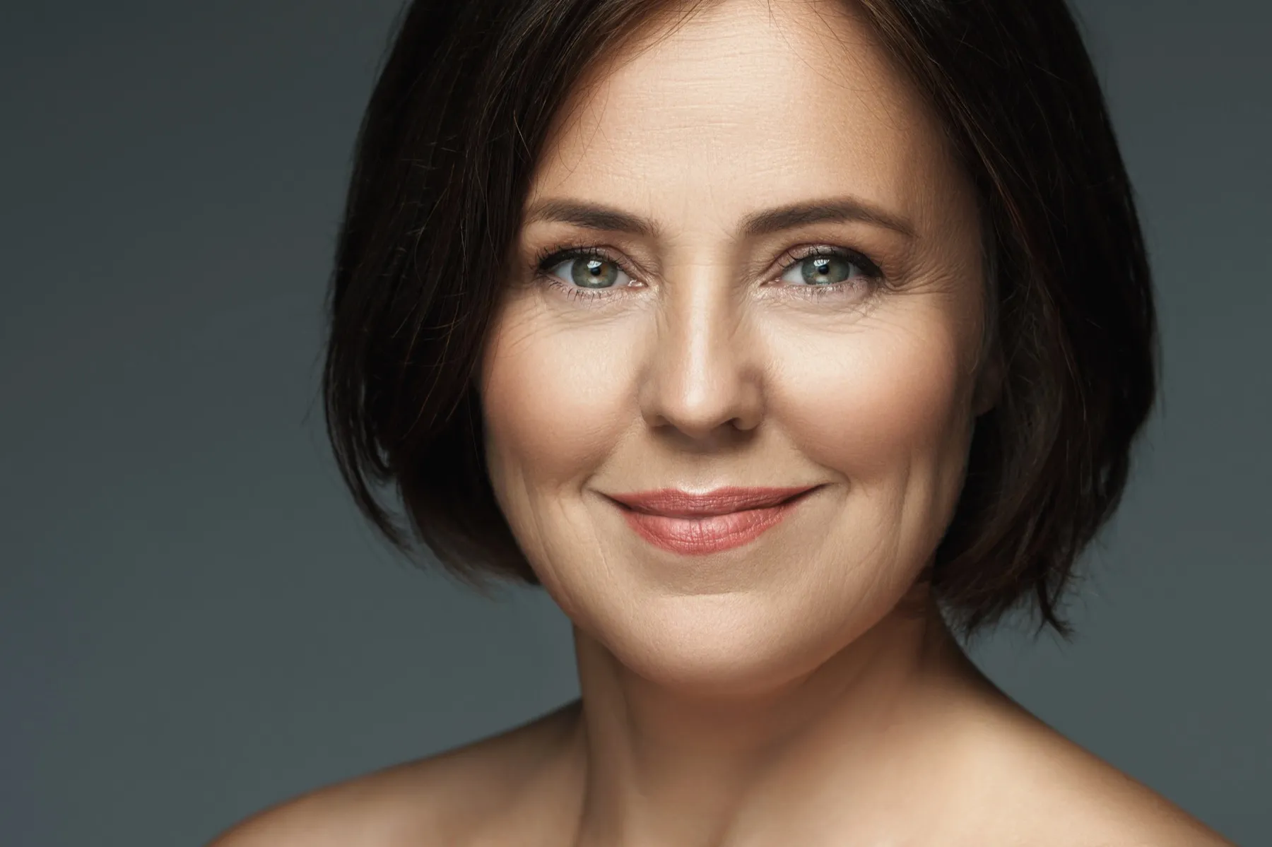 Close-up portrait of a smiling middle-aged woman with short dark hair against a gray background.