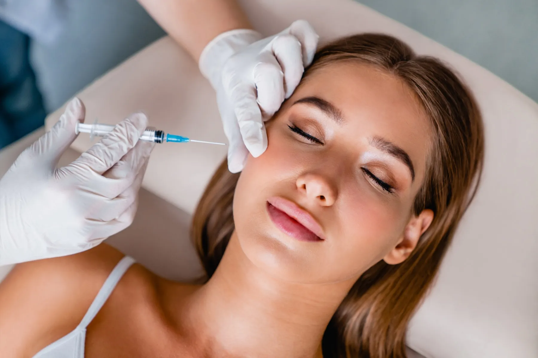 Close-up of a woman with closed eyes receiving a cosmetic facial injection from a gloved professional.