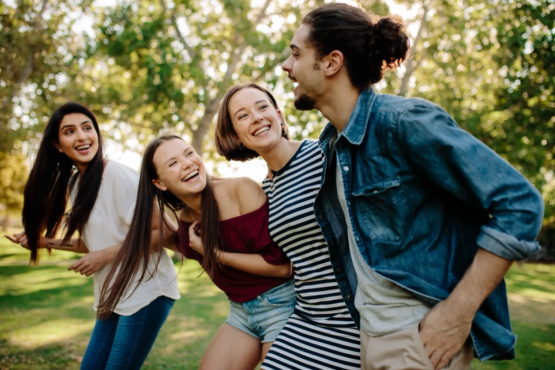 Four young adults outdoors smiling and leaning together with greenery in the background.