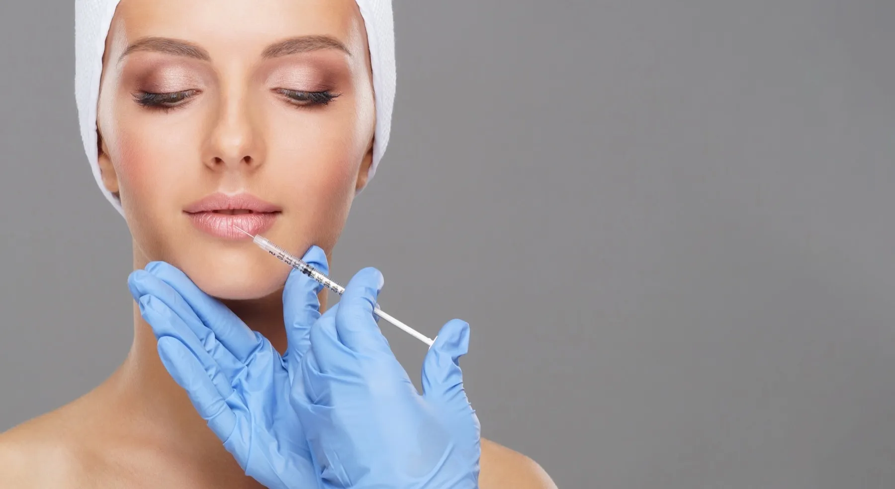 Close-up of a woman with eyes closed receiving a lip injection from a gloved professional.
