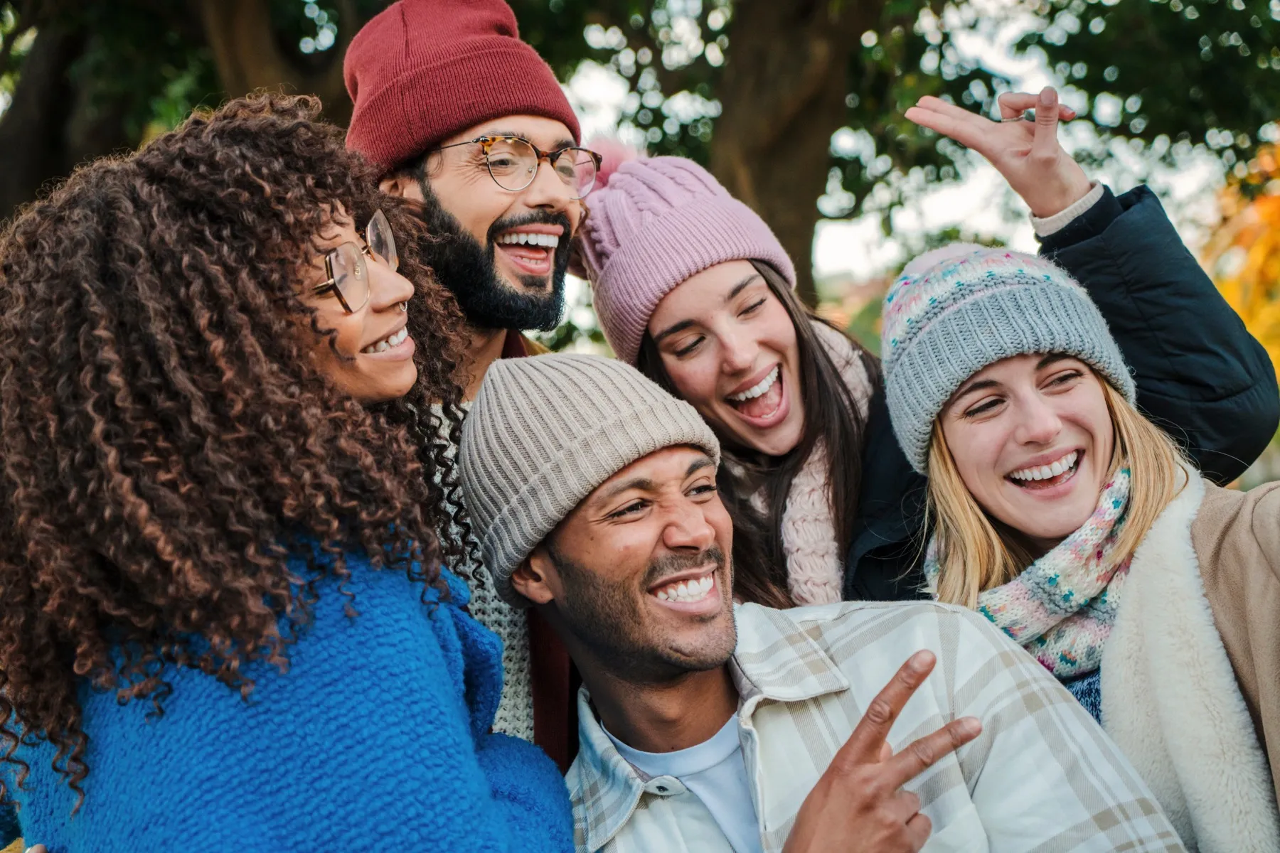Group of five friends wearing winter hats and coats smiling and posing closely for a selfie outdoors.