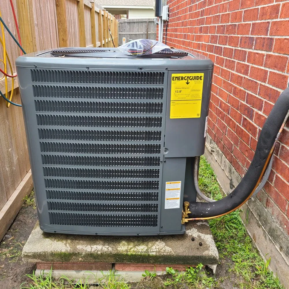 Technician in a hard hat and gloves kneeling while working on wiring inside a commercial HVAC unit outdoors.