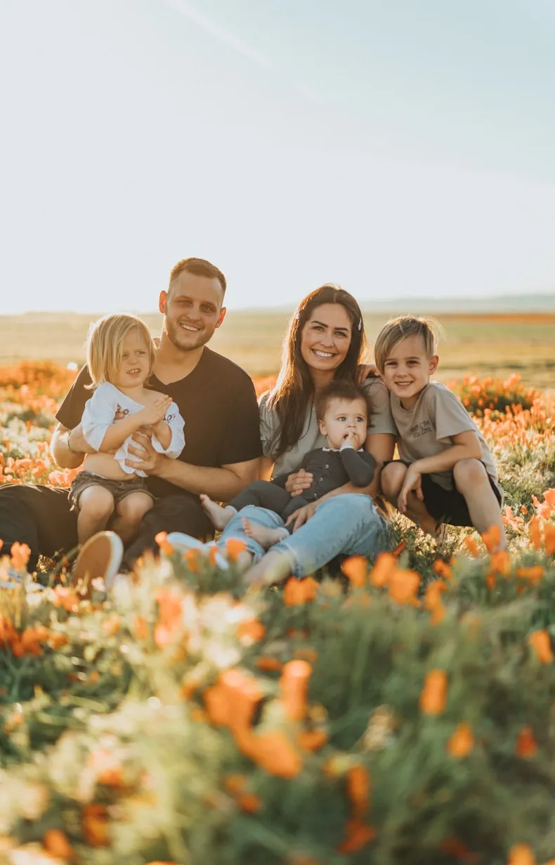 Smiling family of five sitting in a field of orange flowers during golden hour.