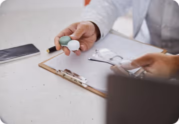 Person in white coat holding two dental aligners over a clipboard with papers and eyeglasses.