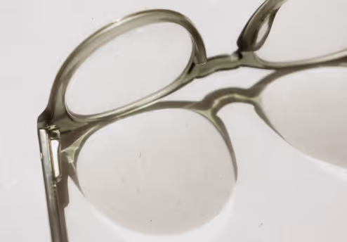 Close-up of translucent light green eyeglass frames casting a shadow on a white surface.