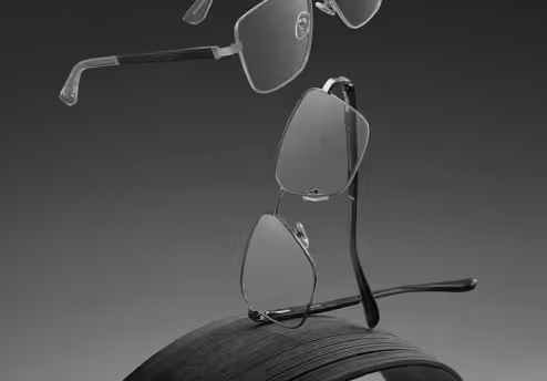 Three pairs of eyeglasses floating above and resting on a textured round object in black and white.