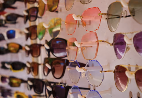 Display of multiple sunglasses with colorful lenses arranged on a wall-mounted rack.