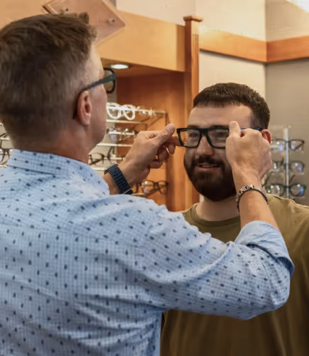 An optician fitting black glasses on a man inside an eyewear store.