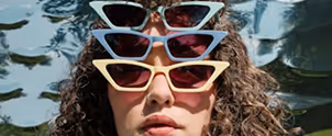 Close-up of a person with short curly hair wearing oversized red translucent sunglasses.