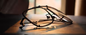 Black-rimmed eyeglasses casting shadow on a wooden surface in warm light.