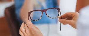 Person holding a pair of tortoiseshell eyeglasses in front of another person.