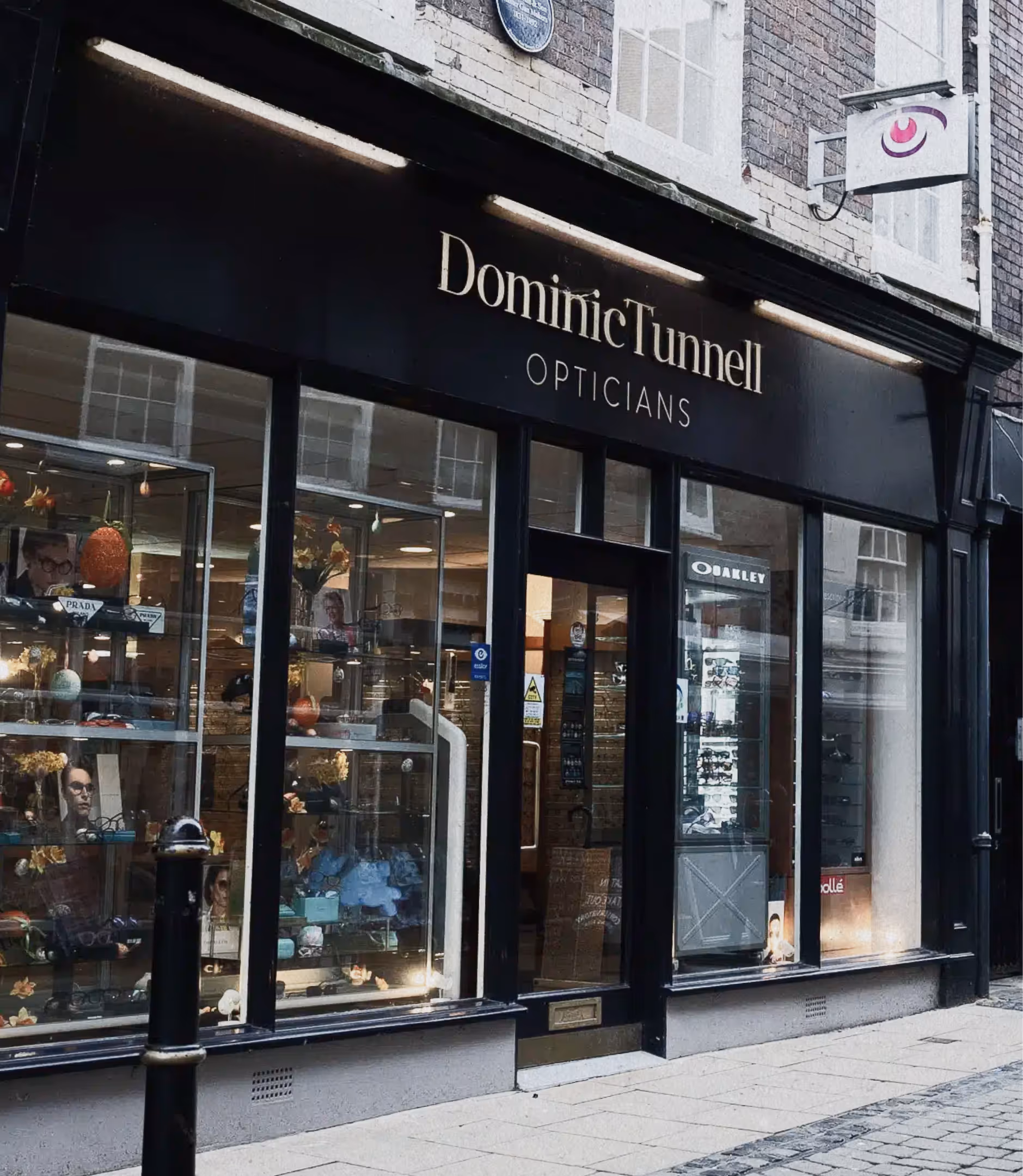 Exterior of Dominic Tunnell Opticians shop with large display windows showing eyewear and accessories.