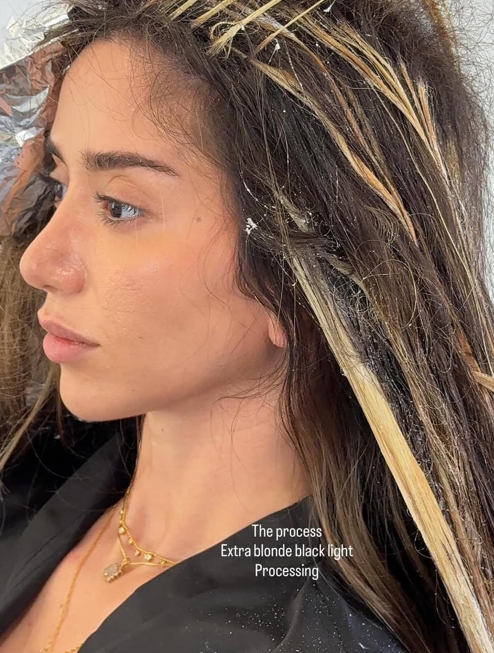 Side profile of a woman with dark hair being lightened with blonde highlights during a hair processing treatment.