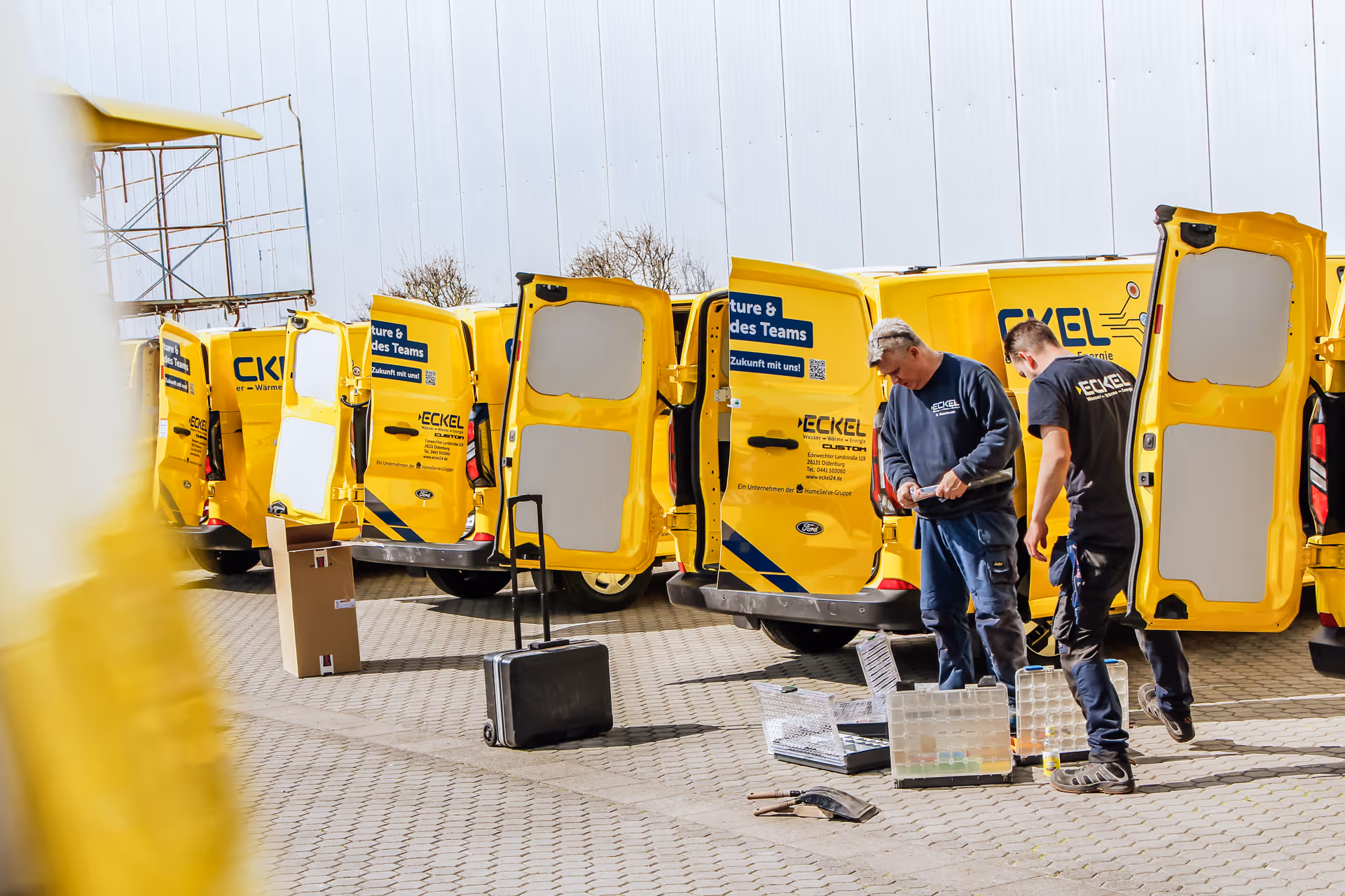 Mehrere gelbe Firmenwagen von Eckel mit geöffneten Hecktüren und Handwerkern