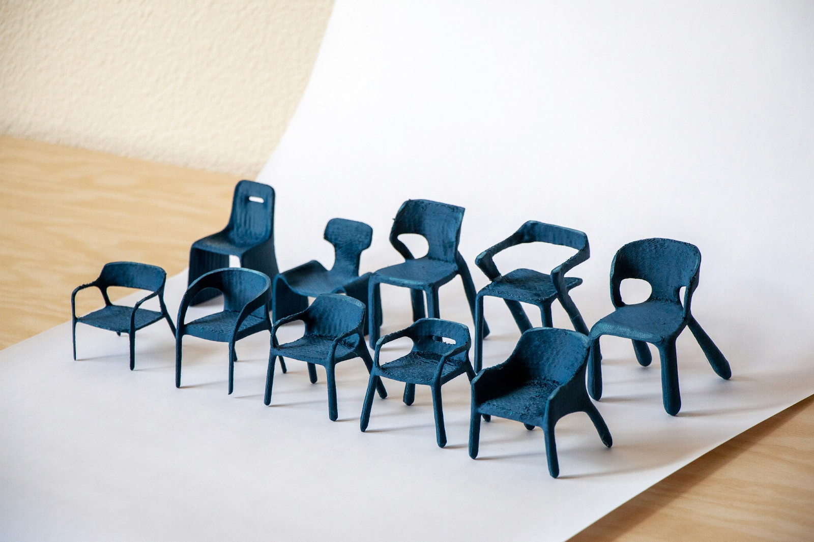 Collection of 3D-printed miniature chair prototypes in dark blue showing varied form explorations