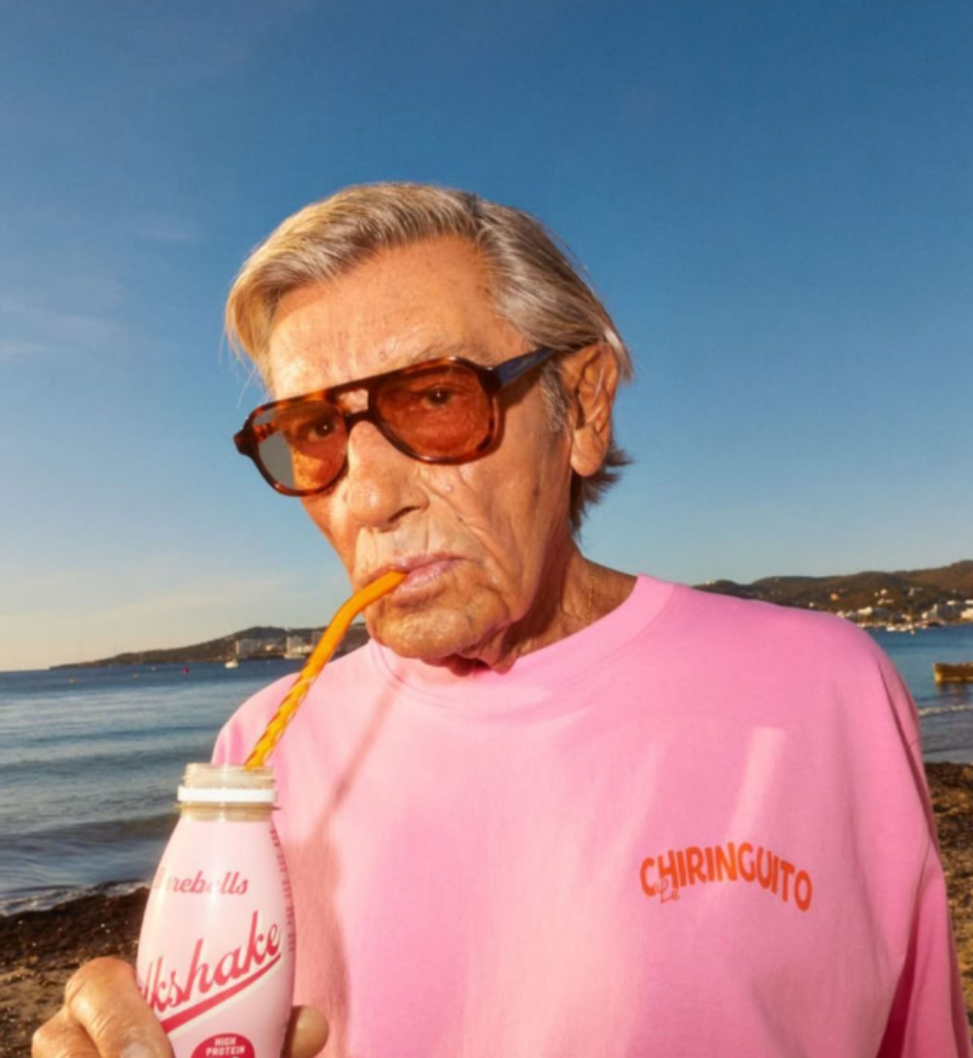 old man wearing a pink sweater with big orange framed glasses